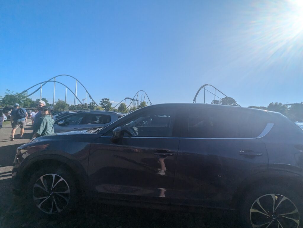 A parked car in front of a rollercoaster