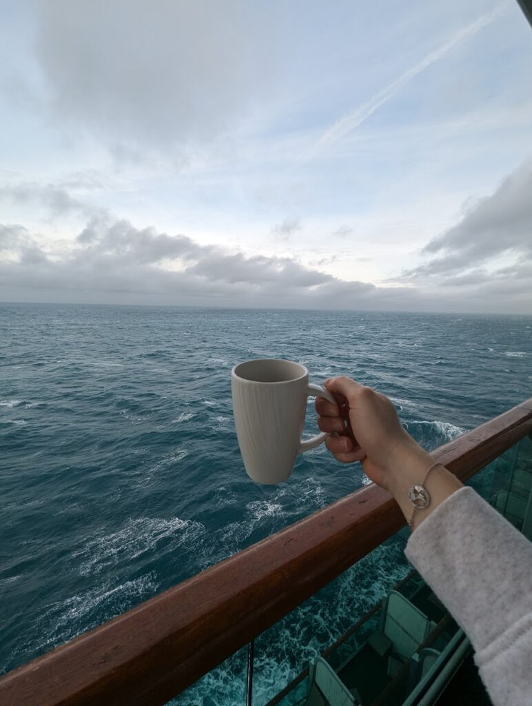 An arm holding a cup of coffee overlooking the sea on a cruise ship balcony